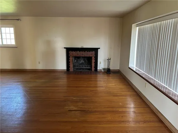 a view of an empty room with wooden floor fireplace and a window