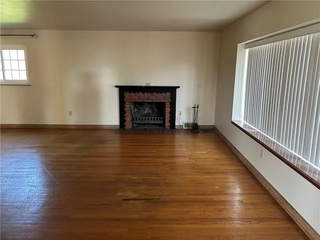 a view of an empty room with wooden floor fireplace and a window