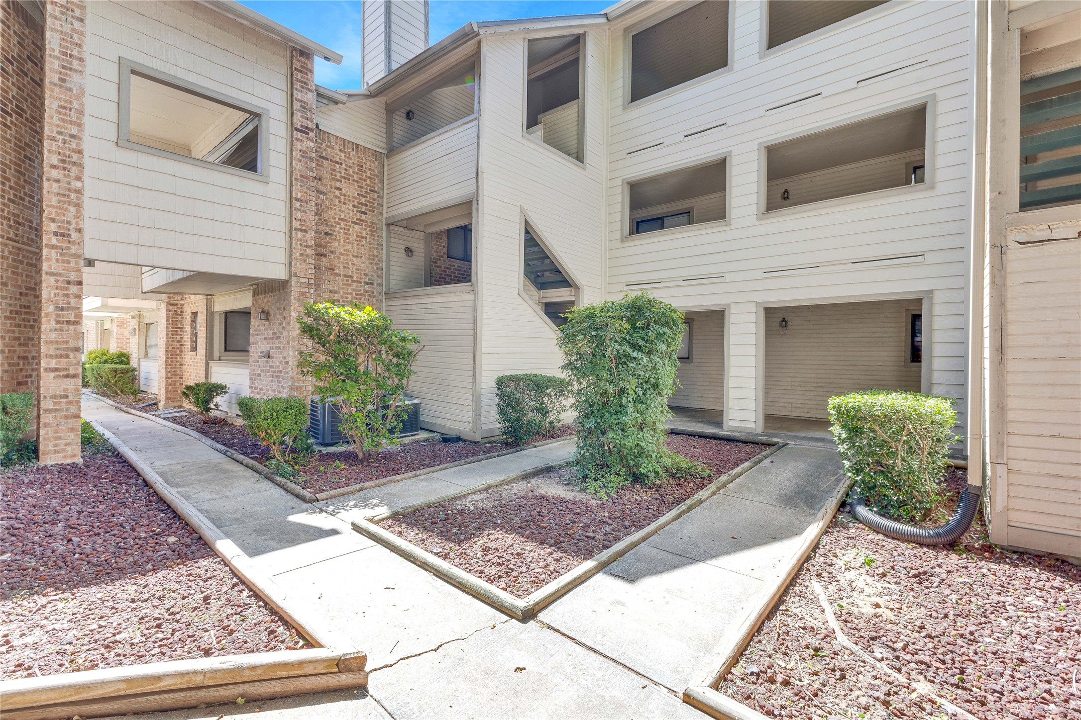2500 Burleson Road, Unit 703 Austin, TX 78741 - Photo 21 of 24 Paved concrete walkways meander through low-maintenance gravel beds outside this multi-level residential building.