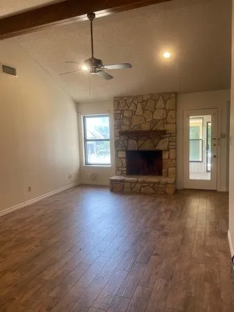 an empty room with wooden floor fireplace and windows