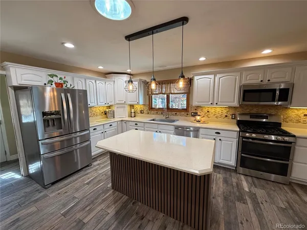a kitchen with stainless steel appliances a refrigerator a stove a sink cabinets and a wooden floor
