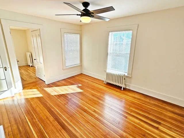 an empty room with wooden floor fan and windows