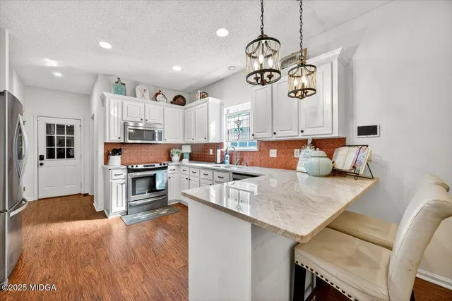 a kitchen with stainless steel appliances granite countertop a stove top oven a sink a dining table and chairs with wooden floor