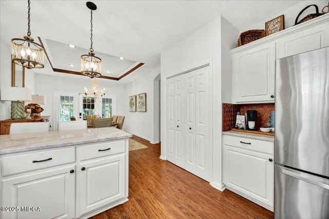 a kitchen with stainless steel appliances granite countertop a refrigerator a sink and white cabinets with wooden floor