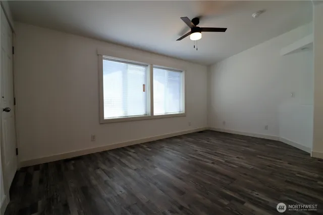an empty room with wooden floor ceiling fan and windows