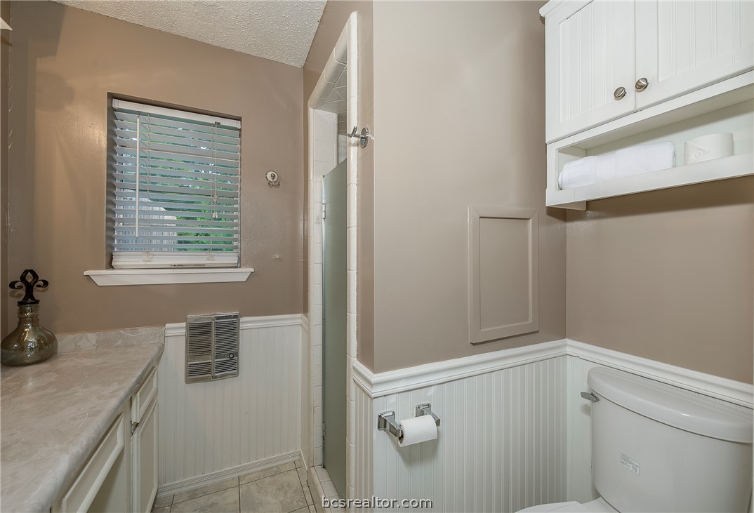 2303 Avon Street Bryan, TX 77802 - Photo 13 of 32 Primary bathroom with wainscoting wall details, painted white cabinets, laminate counter tops & a tiled shower