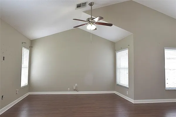 an empty room with wooden floor fan and windows