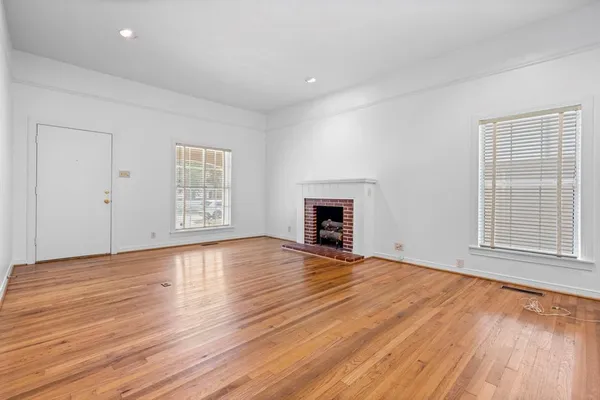 an empty room with wooden floor fireplace and windows