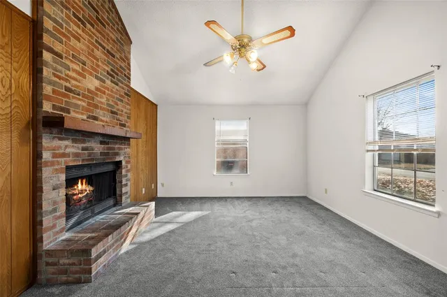 a view of an empty room with chandelier fan and fire place