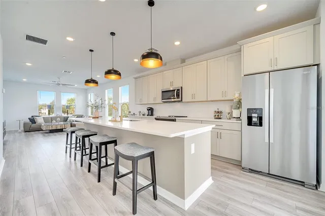 a kitchen with stainless steel appliances kitchen island a refrigerator a stove and white cabinets with wooden floor