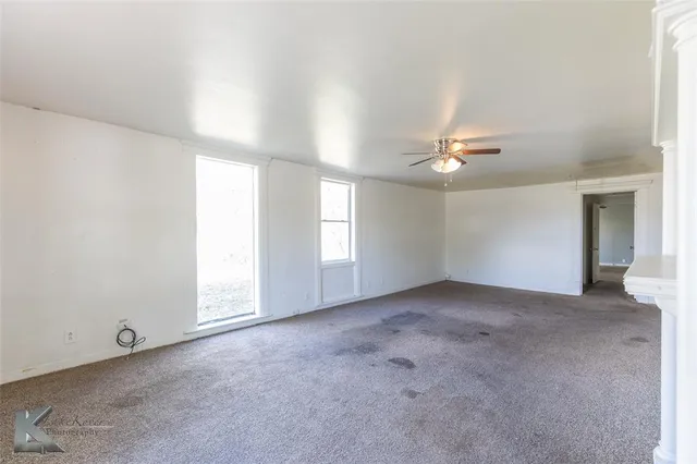 an empty room with windows and chandelier fan