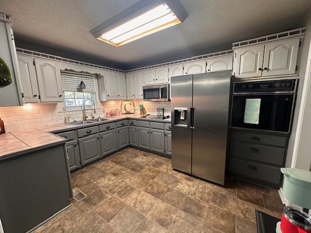 1347 Becton William Road Ripley, TN 38063 - Photo 21 of 24 Dual tone kitchen featuring tile countertops, stone finish flooring, black appliances, a textured ceiling, and decorative backsplash