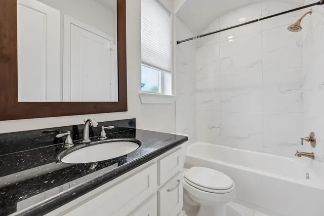 a bathroom with a granite countertop sink a toilet a mirror a bathtub and shower