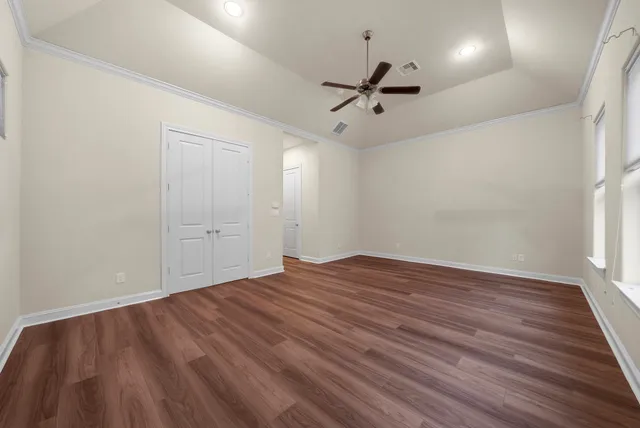 an empty room with wooden floor a ceiling fan and kitchen view