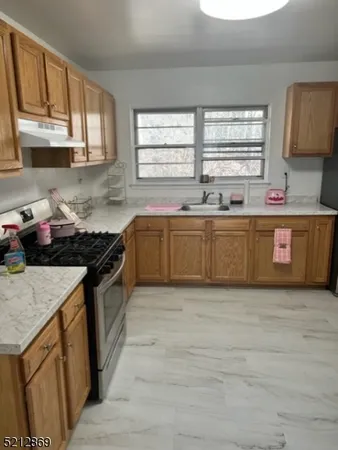 a large kitchen with granite countertop a stove top oven a sink a window and wooden cabinets