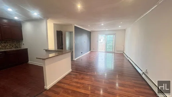 a view of an empty room with wooden floor and a kitchen