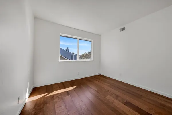a view of an empty room with wooden floor and a window