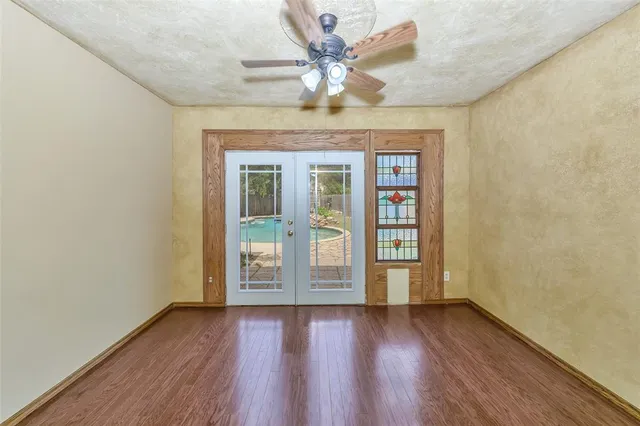an empty room with wooden floor chandelier fan and windows