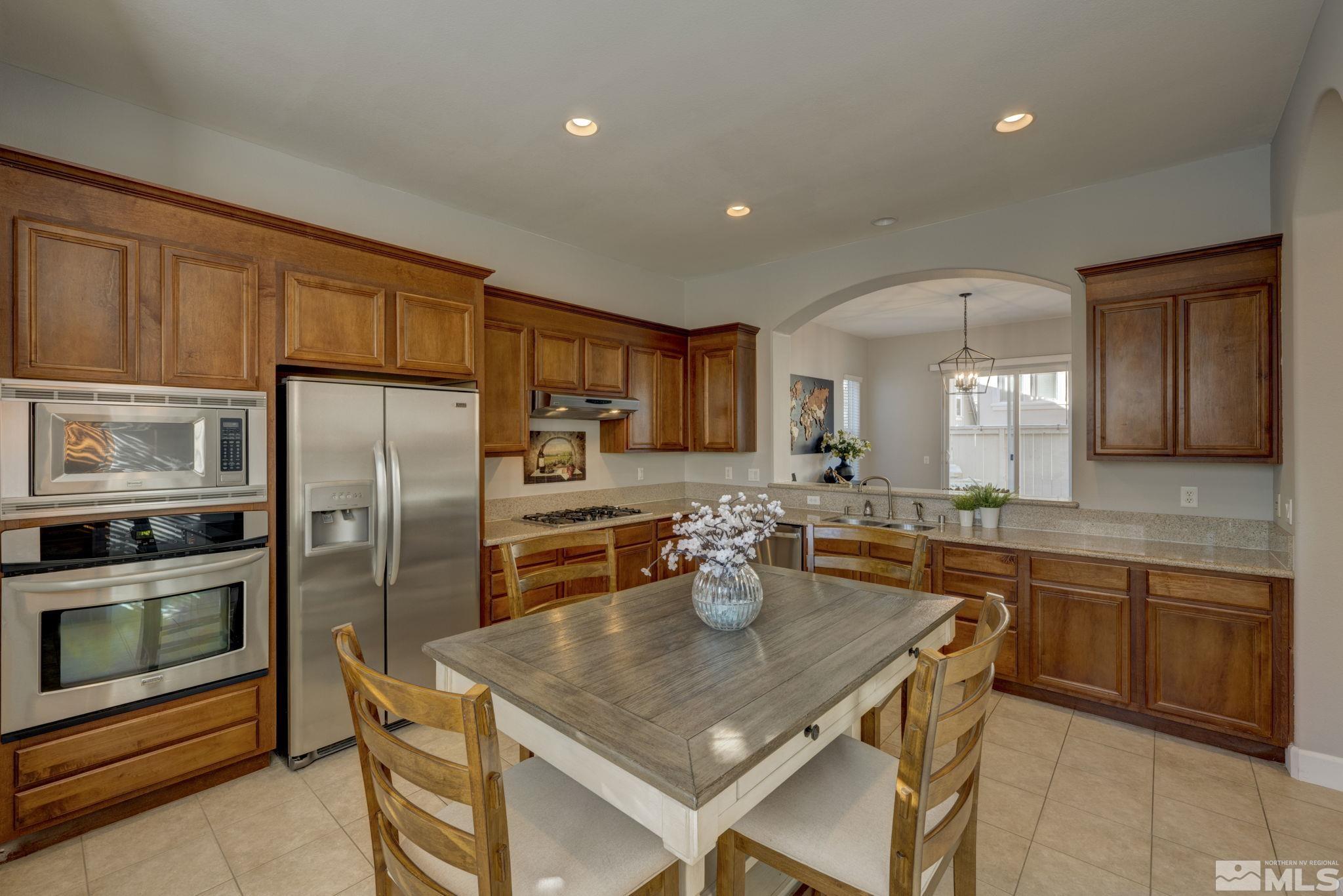 7669 Stone Bluff Way Reno, NV 89523 - Photo 12 of 40 a kitchen with a refrigerator a sink dishwasher a stove and a dining table with wooden cabinet