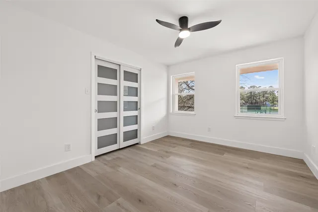 an empty room with wooden floor chandelier fan and windows