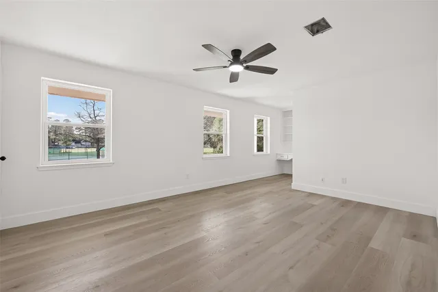 a view of empty room with wooden floor and fan