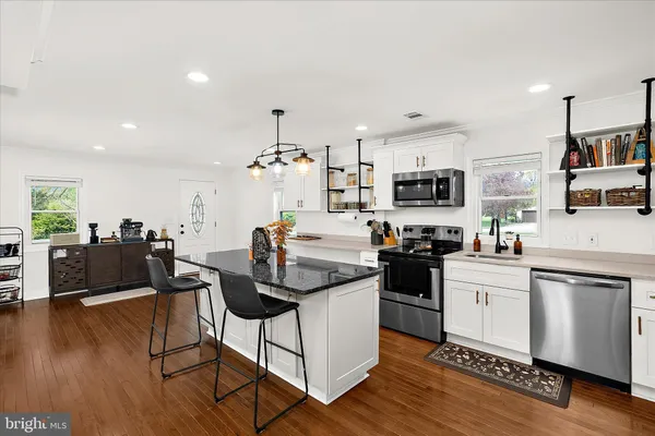 a kitchen with stainless steel appliances kitchen island granite countertop a stove top oven a sink a dining table and chairs with wooden floor