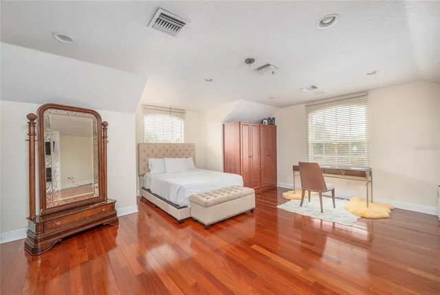 a spacious bedroom with a bed a table and wooden floor