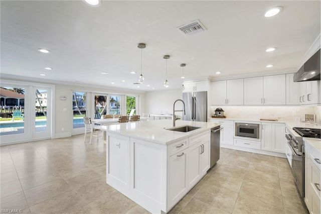 a large white kitchen with a stove top oven a sink a dining table and chairs