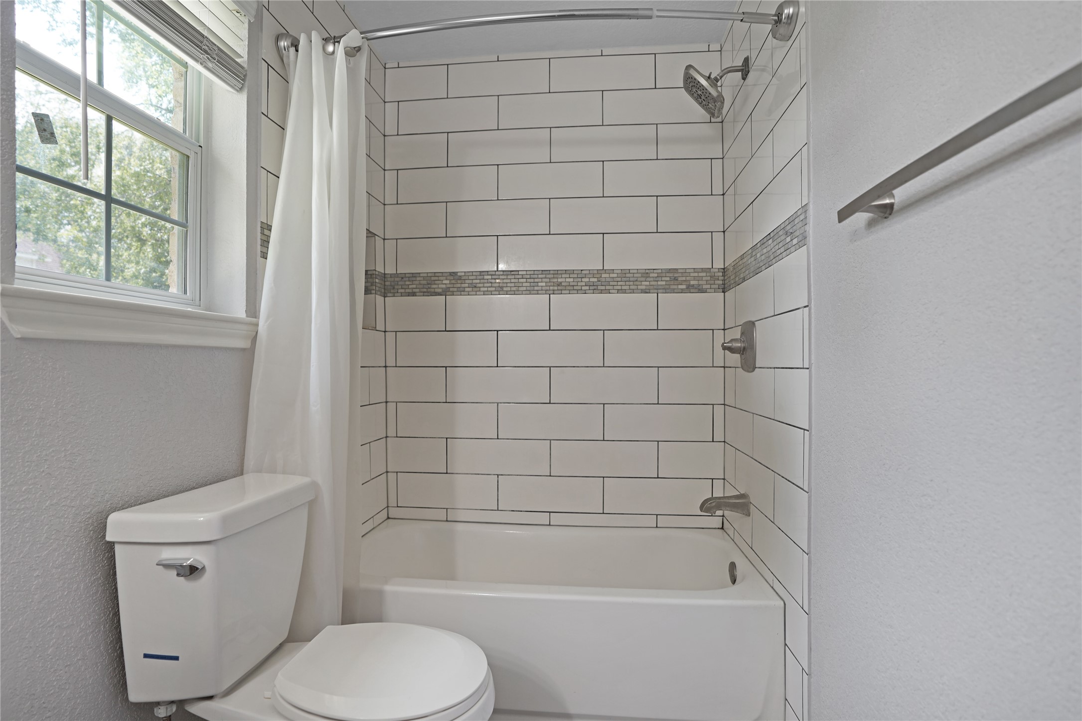 17119 Mellow Ridge Drive Spring, TX 77379 - Photo 20 of 32 This bathroom features a clean, modern design with a white tiled shower and bathtub, complemented by a slim accent strip. Natural light streams in through a window, and there's a sleek towel bar on the wall.