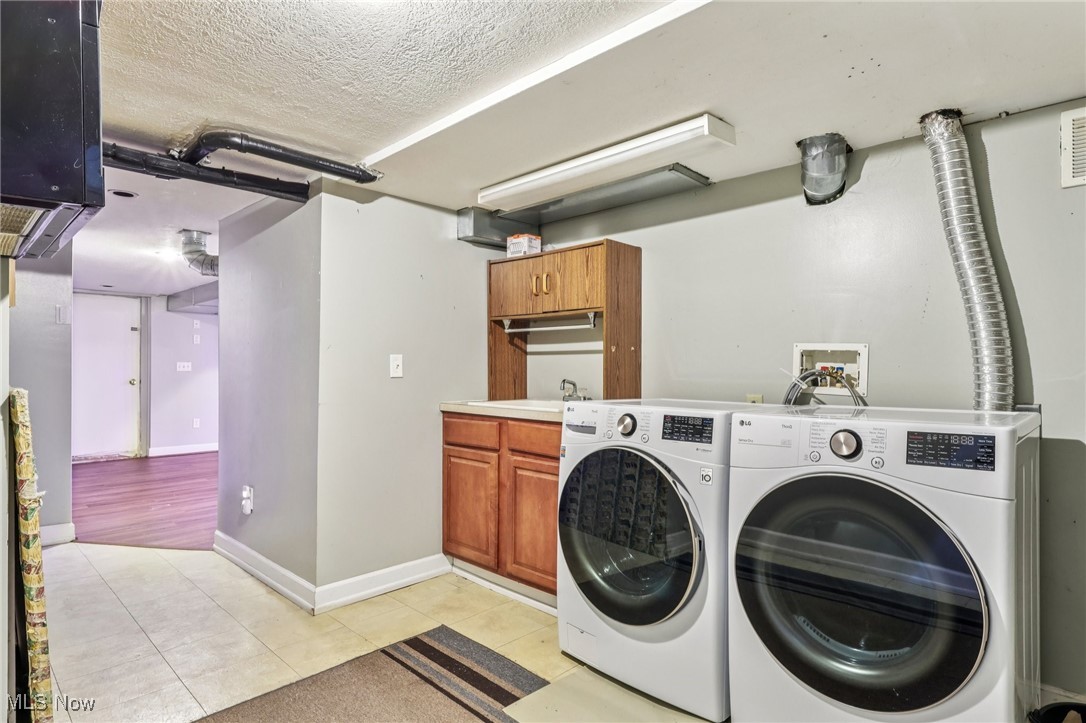 23 Lane Street Rittman, OH 44270 - Photo 13 of 34 Laundry room with light tile patterned floors, a textured ceiling, washer and clothes dryer, and cabinet space