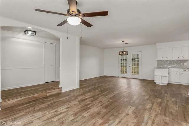an empty room with wooden floor chandelier fan and windows