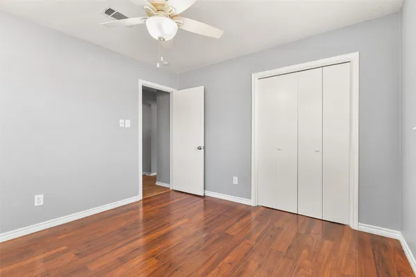 a view of an empty room with wooden floor and a ceiling fan