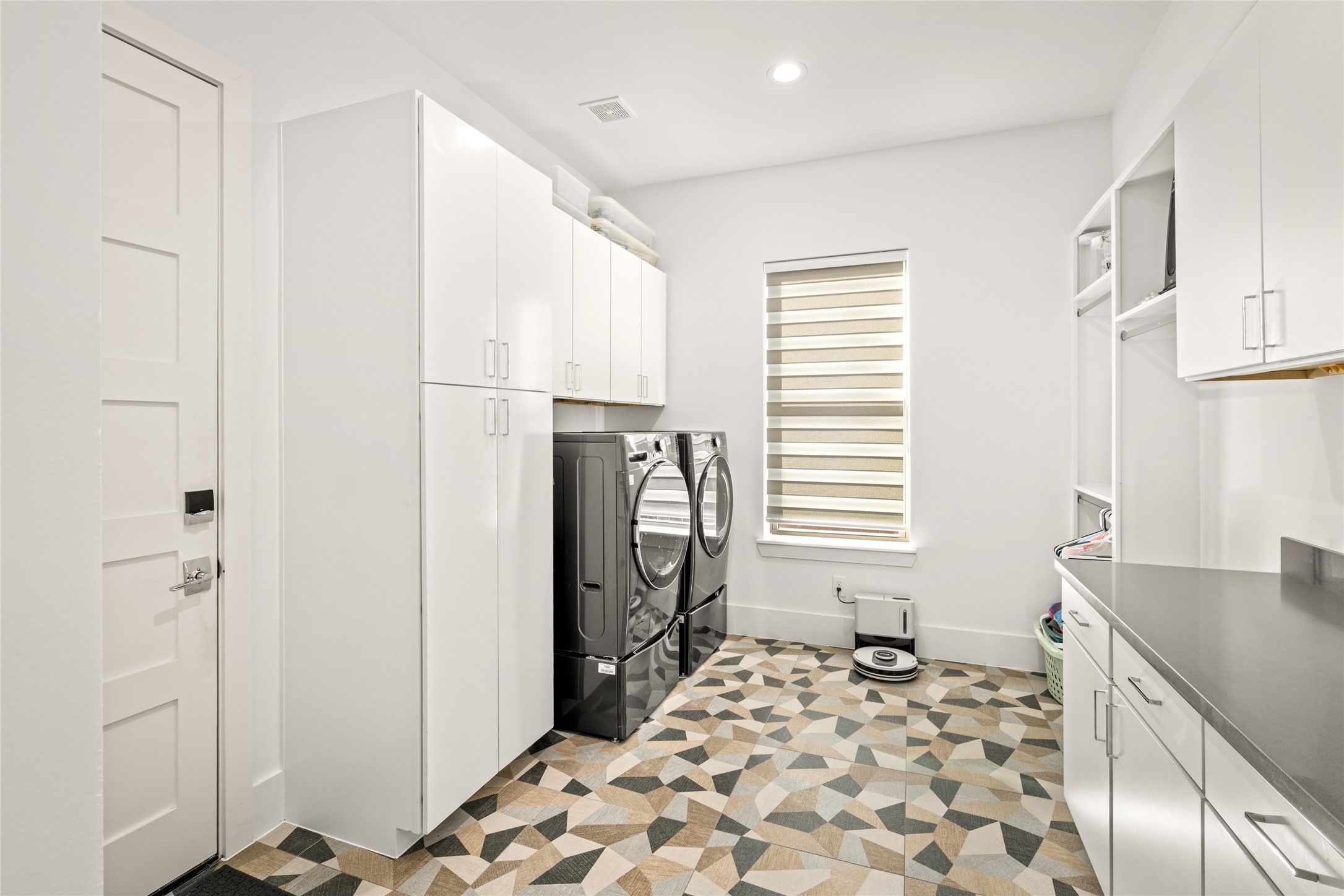 5706 Birdwood Road Houston, TX 77096 - Photo 19 of 50 This spacious laundry room features ample white cabinetry for storage, lots of counter space and drawers, hanging area and a decorative, geometric tile floor. Natural light filters into the room through the custom window blind, creating an enjoyable, bright and functional space. Recessed lighting adds additional light. Door to the left leads out to the 3-car, tandem garage with high ceilings.