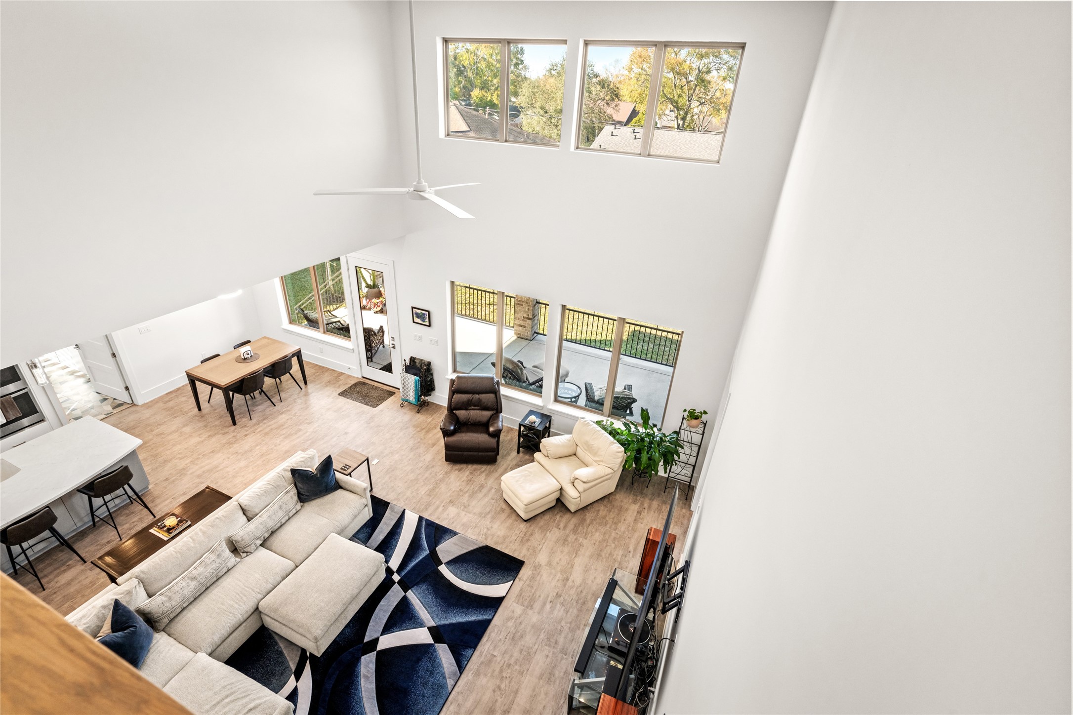 5706 Birdwood Road Houston, TX 77096 - Photo 29 of 50 A view from the upstairs catwalk capturing the spacious living area features high ceilings, large clerestory windows for natural light, and an open layout. It includes a view of the breakfast area, modern kitchen with bar seating, dining space, and access to the outdoor patio, perfect for entertaining and family gatherings.