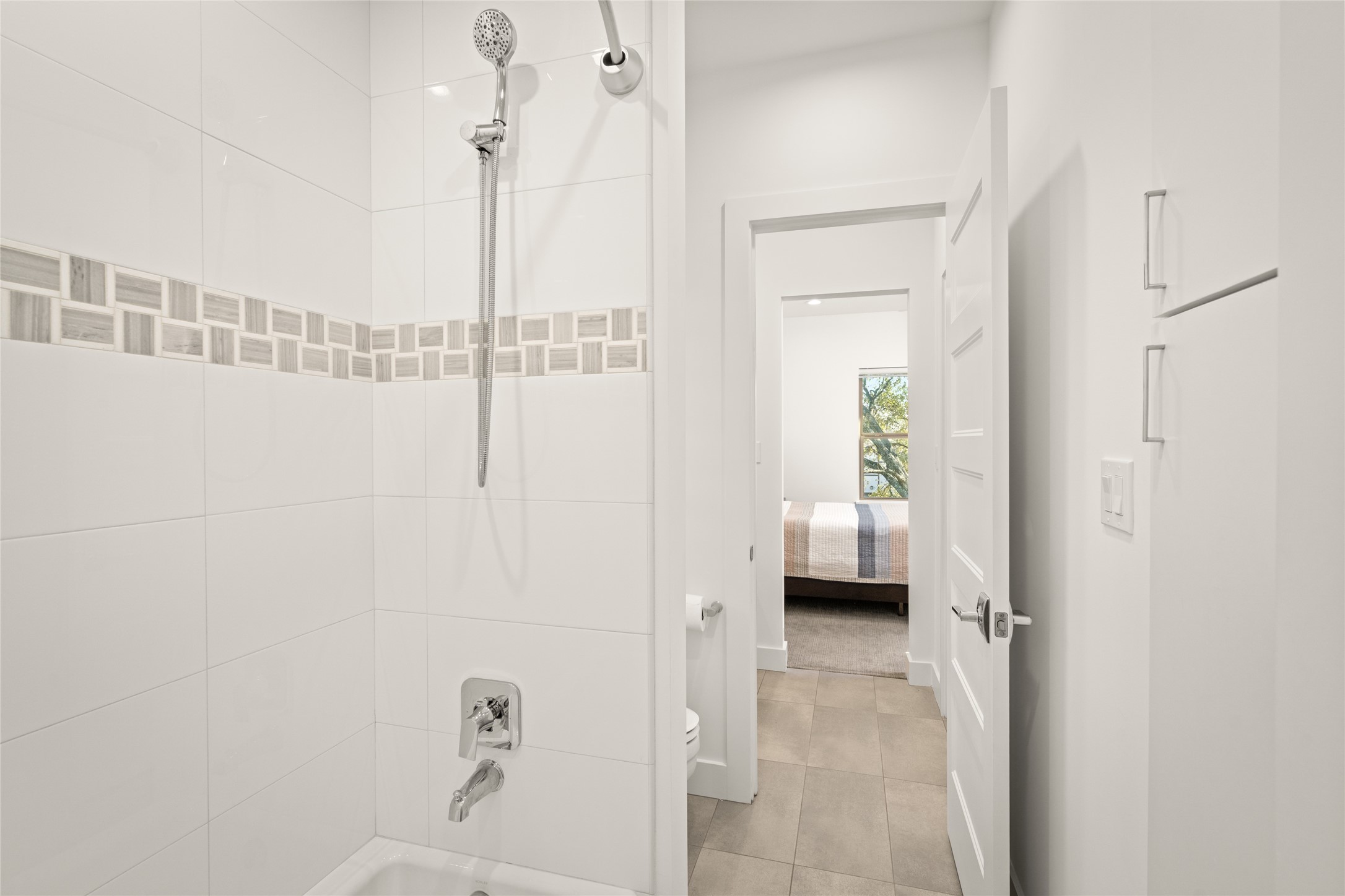 5706 Birdwood Road Houston, TX 77096 - Photo 34 of 50 This photo showcases the tub bath shared in between bedroom 2 and 3. There are two private vanities with doors on either side. The shower features a handheld showerhead and decorative tiling to the ceiling. The space leads into one of the secondary bedrooms, creating a seamless flow between the rooms.