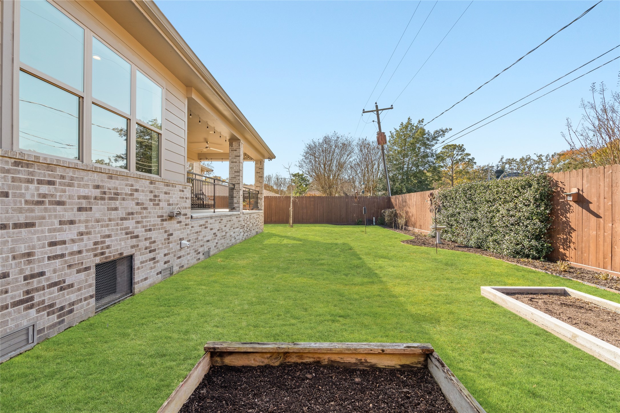 5706 Birdwood Road Houston, TX 77096 - Photo 43 of 50 Backyard with a neatly maintained lawn, surrounded by a wooden fence for privacy. The house features a brick exterior and large windows, with a covered patio area perfect for outdoor gatherings. Raised garden beds add potential for gardening enthusiasts. Almost ready for planting!