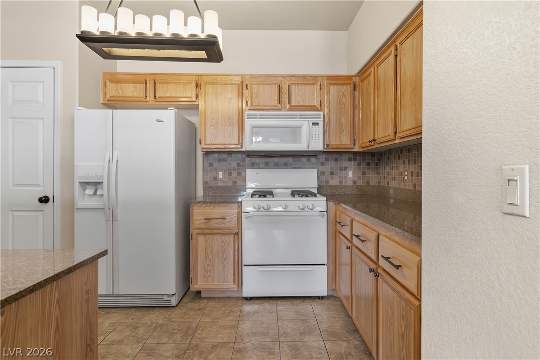 10550 West Alexander Road, Unit 2060 Las Vegas, NV 89129 - Photo 16 of 45 Well-equipped kitchen features ample wood cabinetry, patterned tile backsplash, and durable countertops.