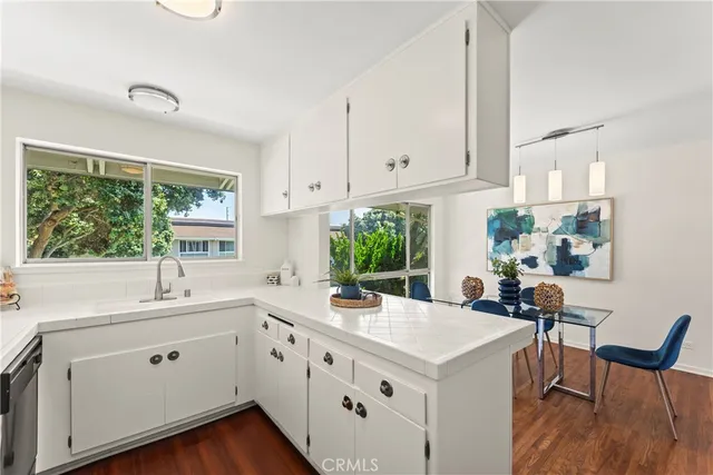 a kitchen with a stove a sink and white cabinets with wooden floor next to windows