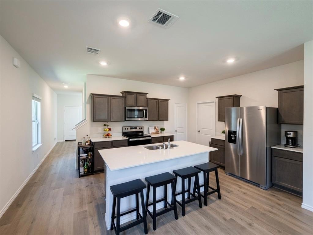 816 Country Road Royse City, TX 75189 - Photo 2 of 24 Contemporary kitchen featuring a large central island with a sink, grey cabinetry, stainless steel appliances, and light wood-finish flooring