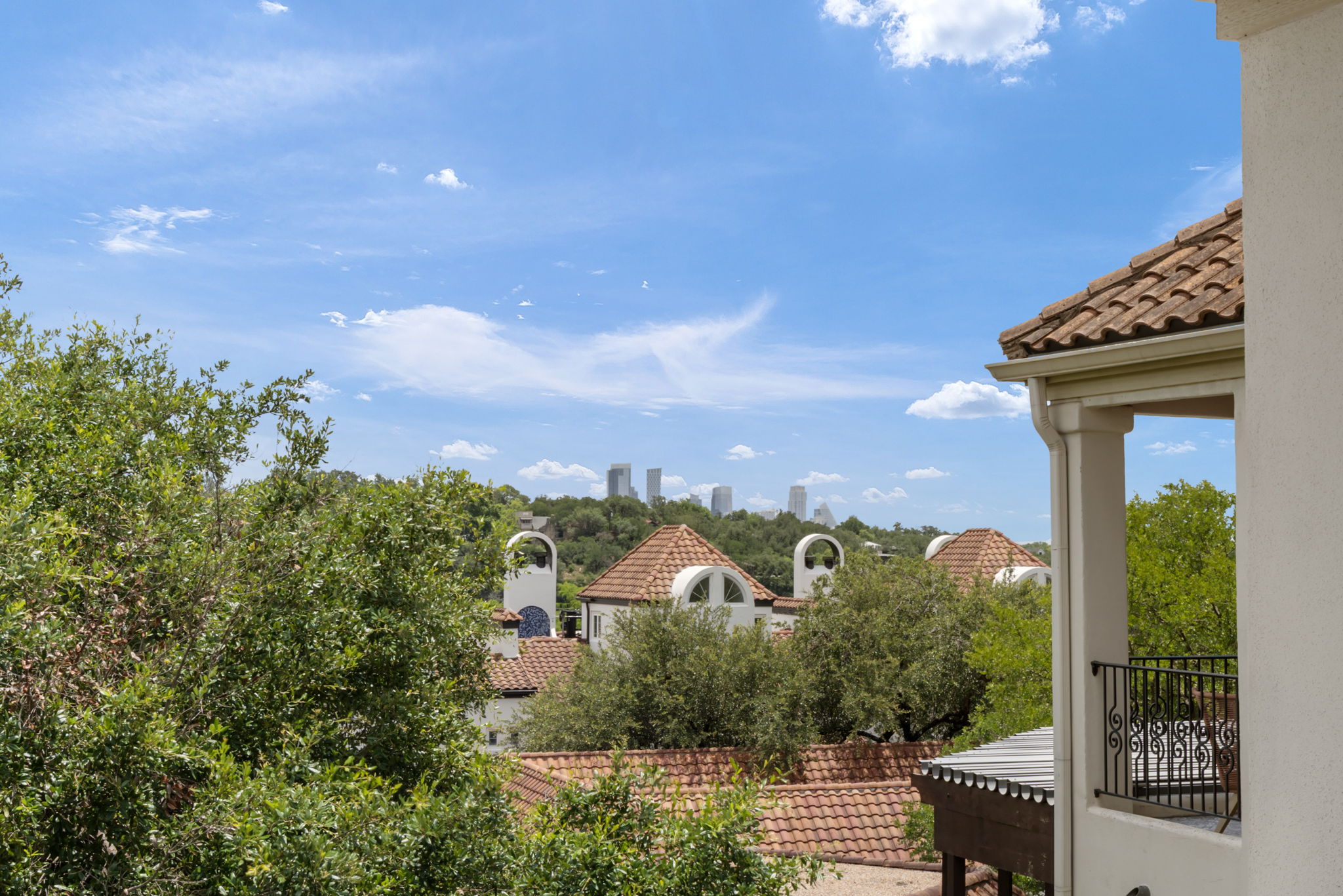 1910 Rue De St Tropez, Unit 6 Austin, TX 78746 - Photo 3 of 37 A terracotta tiled roof offers city skyline views, framed by green treetops and a sunny sky.