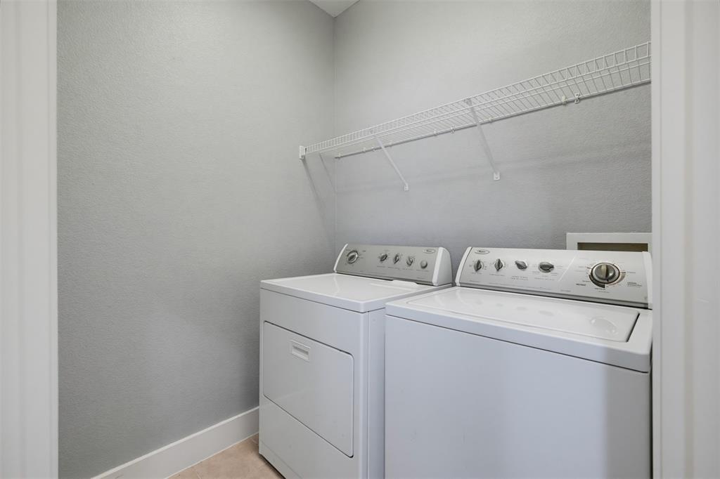 4830 Cedar Springs Road, Unit 30 Dallas, TX 75219 - Photo 31 of 32 Dedicated laundry area featuring a white washer and dryer set, overhead wire shelving, light gray wall finish, and neutral flooring