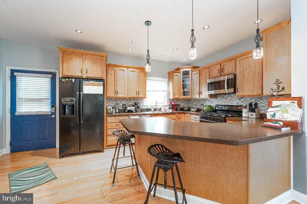 a kitchen with stainless steel appliances granite countertop a refrigerator a sink dishwasher a stove and a dining table with wooden floor