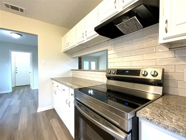 a kitchen with granite countertop wooden floors stainless steel appliances a sink and cabinets