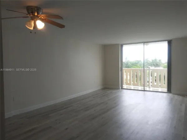 a view of an empty room with wooden floor and a ceiling fan