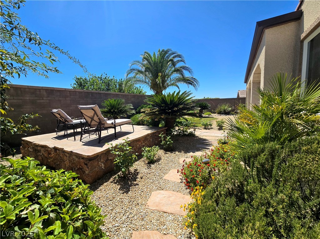2567 Dirleton Place Henderson, NV 89044 - Photo 56 of 67 A desert oasis backyard with a paved sun deck and a lush garden of palm trees and flowering shrubs.