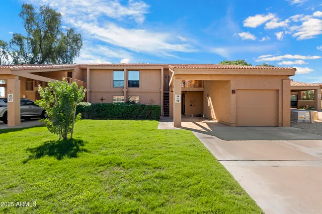 a view of a white house with a yard plants and a large tree