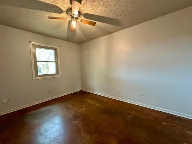 an empty room with wooden floor chandelier fan and windows