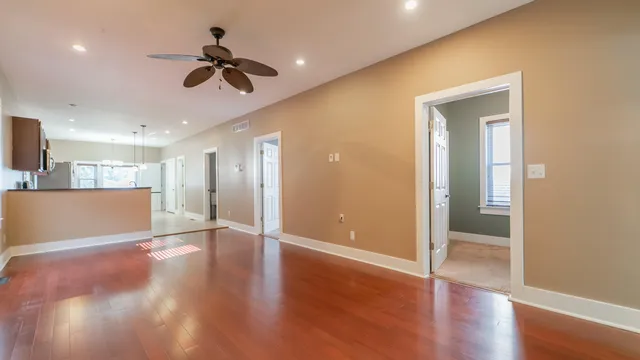 a view of an empty room with wooden floor and a ceiling fan