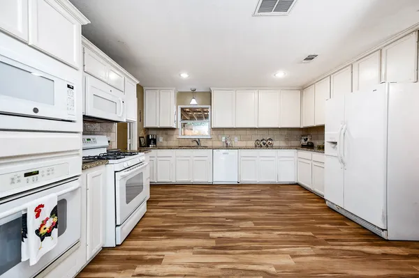 a large kitchen with stainless steel appliances granite countertop a stove a sink and white cabinets
