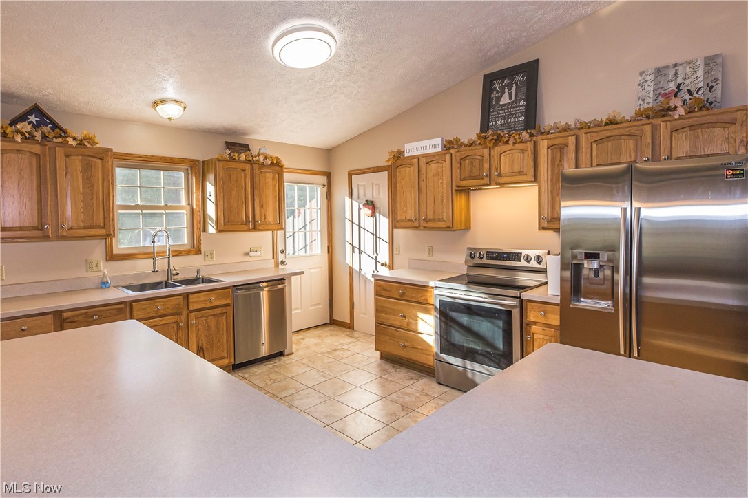 1804 Grace Road Akron, OH 44312 - Photo 4 of 15 Kitchen with a textured ceiling, brown cabinets, light countertops, appliances with stainless steel finishes, lofted ceiling, and light tile flooring